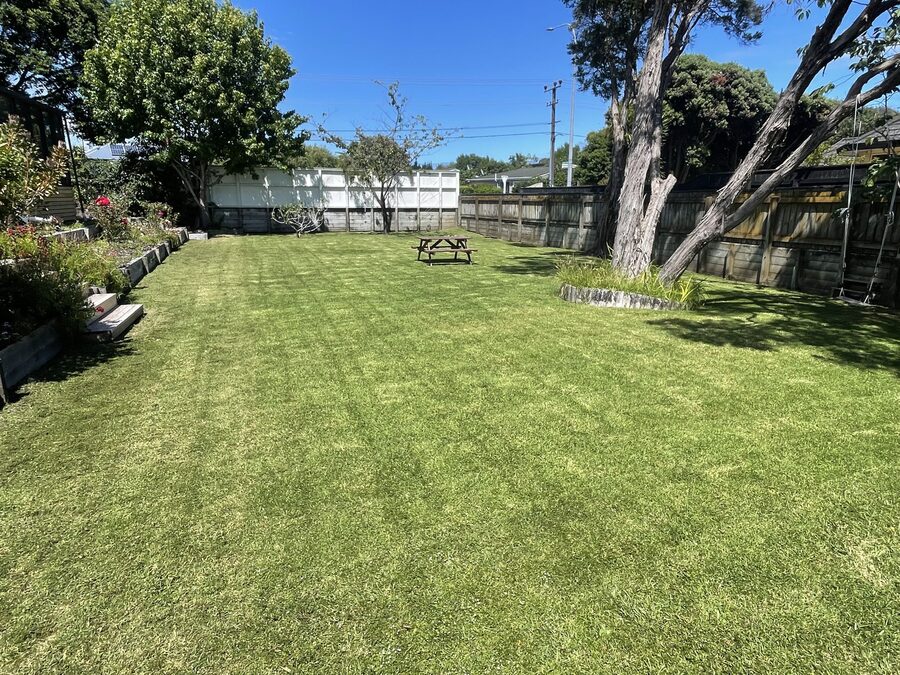 A long manicured lawn with a picnic table and flower beds